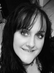 Black and white close up face photo of smiling slave joy with dark long hair and bangs with a silver infinity collar.