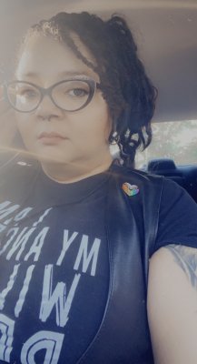 Selfie picture of Honey in a leather vest, "Queer AF" pin, and a shirt that reads "I am my ancestor's wildest dream".