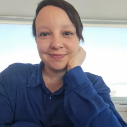 Madame Selana wearing a blue shirt, looking at the camera and smiling.