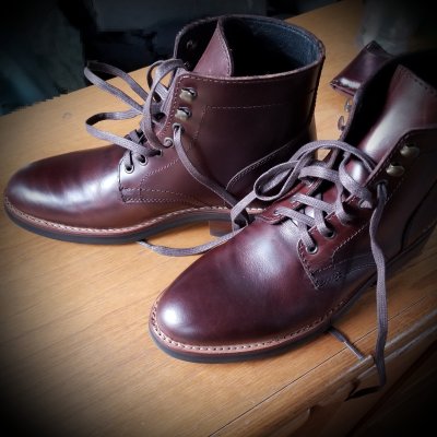 A pair of dark brown boots on a light brown table. The image is square, but with a corners shaded black creating a circular vibe