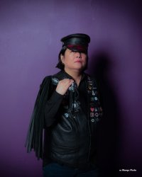 Portrait photograph of person wearing Muir cap and black clothing with a purple background.